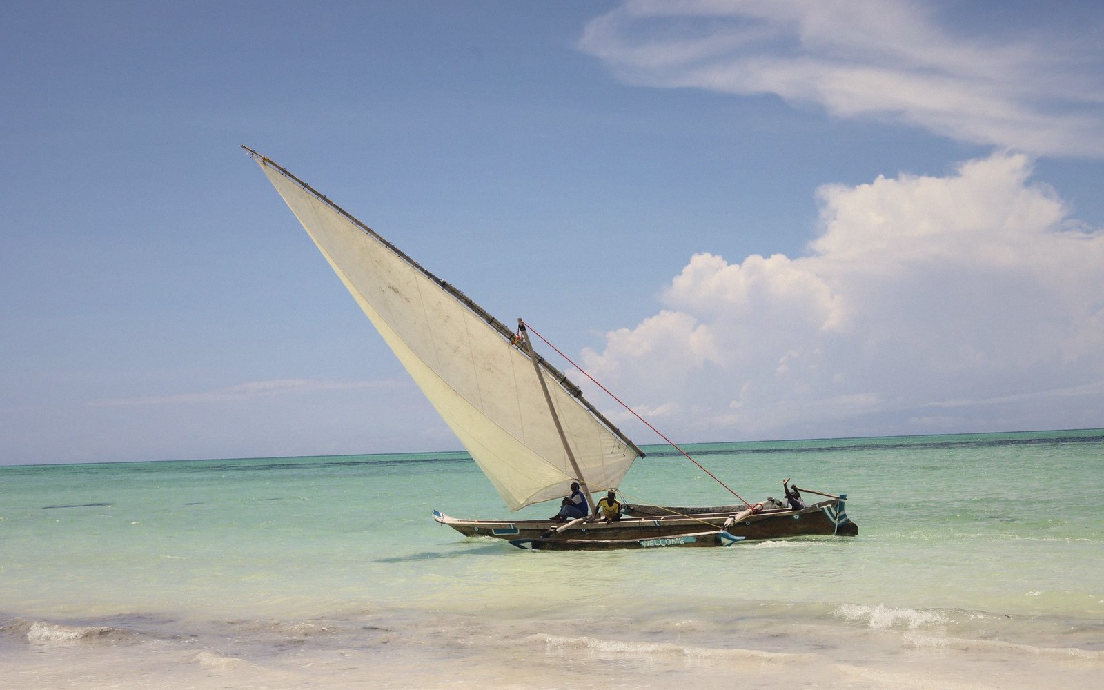 A traditional dhow with triangular sail carries passengers across shallow turquoise water